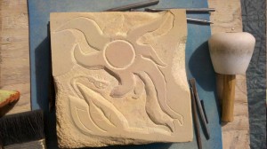 Depiction of sun with flowers on stone.